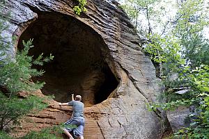 Jay scaling a tree-branch-ladder to look inside a cave.