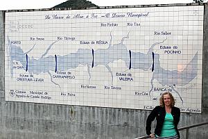 Back in Regua, Kyleen posing for a photo in front of a map that illustrates the five dams along the Douro River.